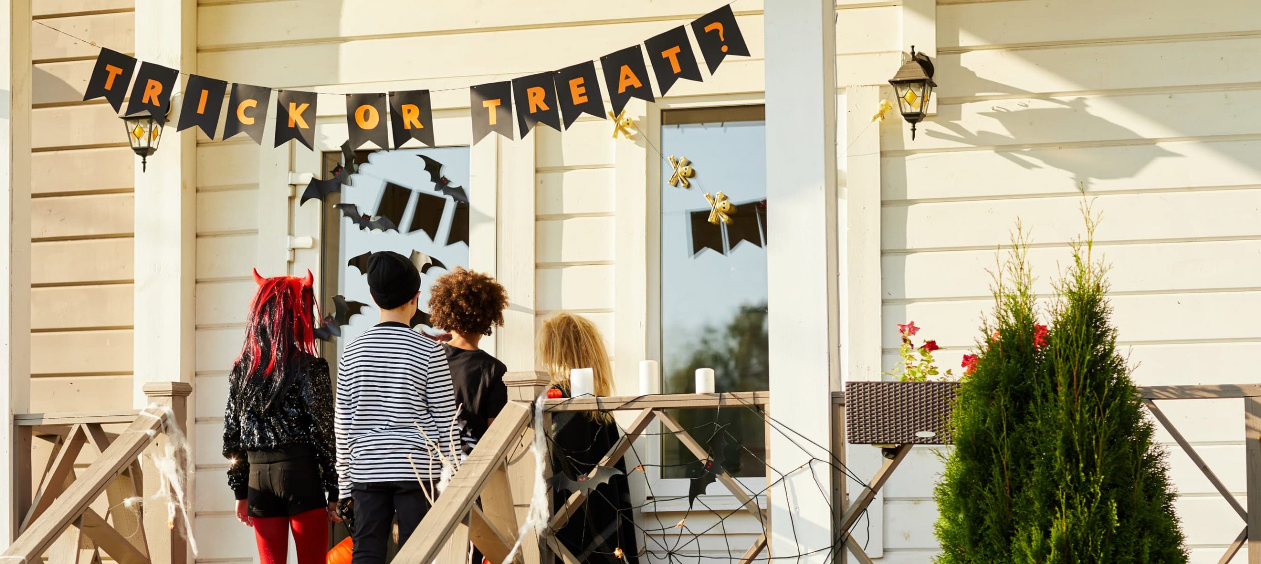 Back view of children trick or treating on Halloween, kids standing on porch knocking on doors of decorated house, copy space