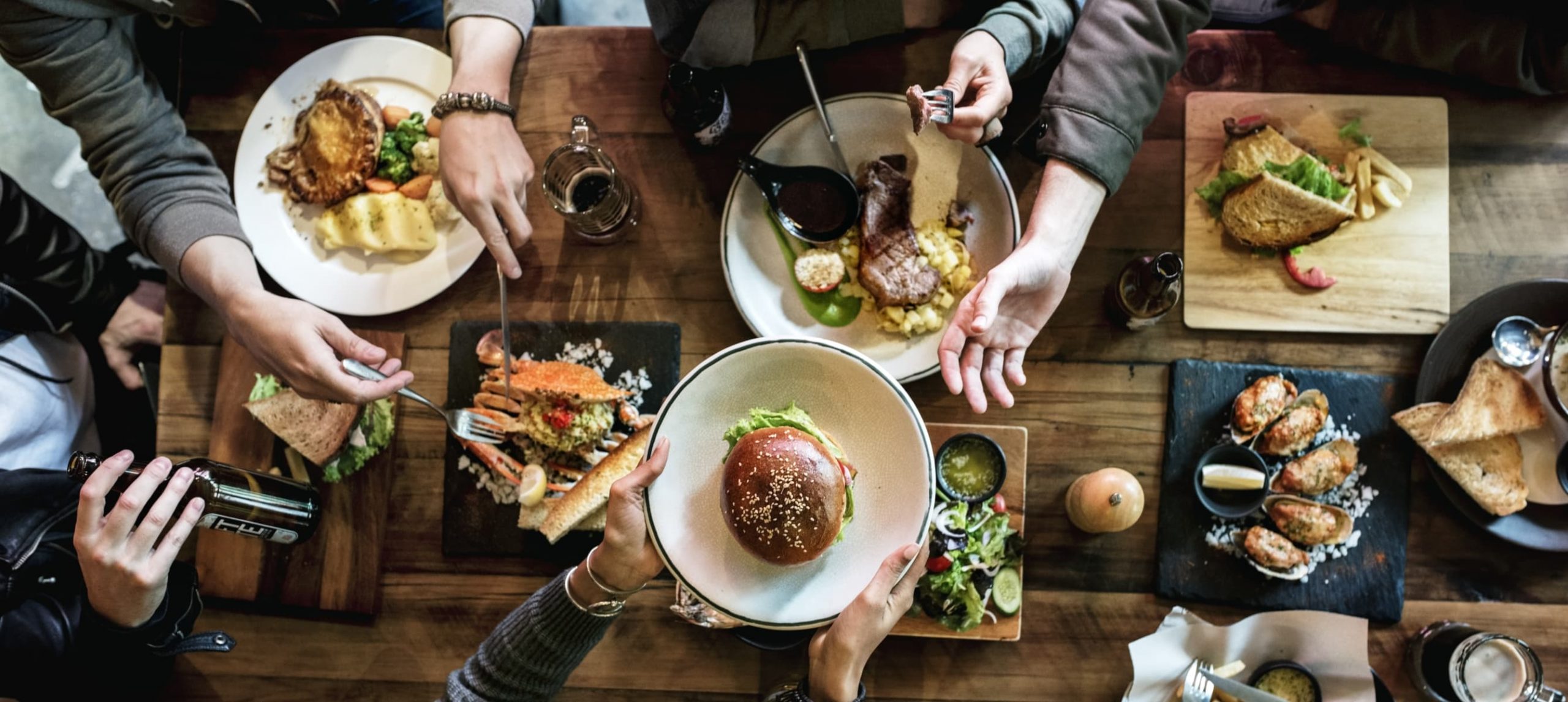 A group of friends having a meal at a large wooden table at a restaurant.