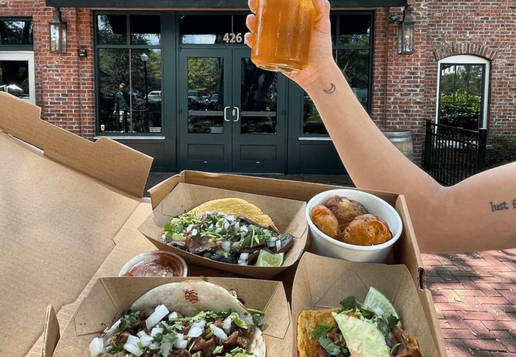 Young woman holding two boxes of tacos and a glass of cold beer at Hunder Street Tacos.