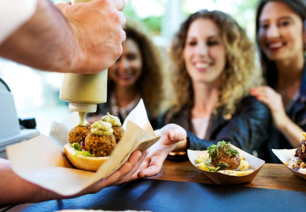 Three young women grabing a falafel sandwich at a food truck.