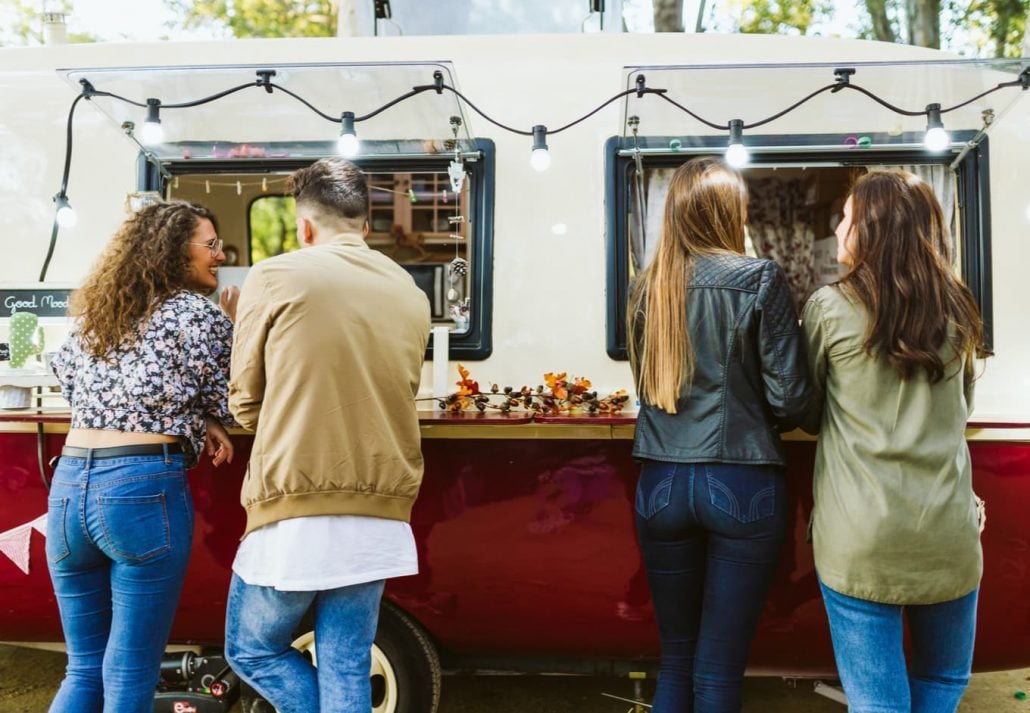 Three young women and a guy at a food truck grabing their order and talking to each other.