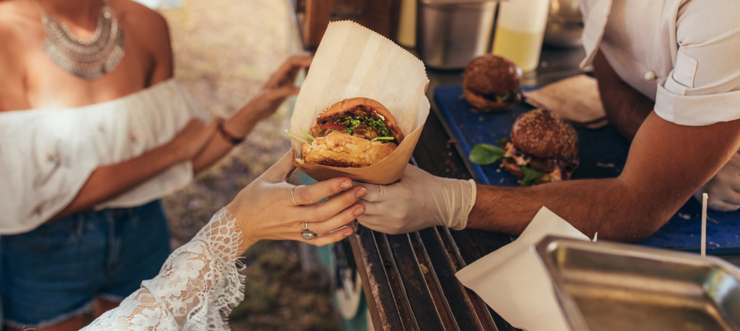 Close yp of two young lady's hands gettin their hamburgers at a food truck.