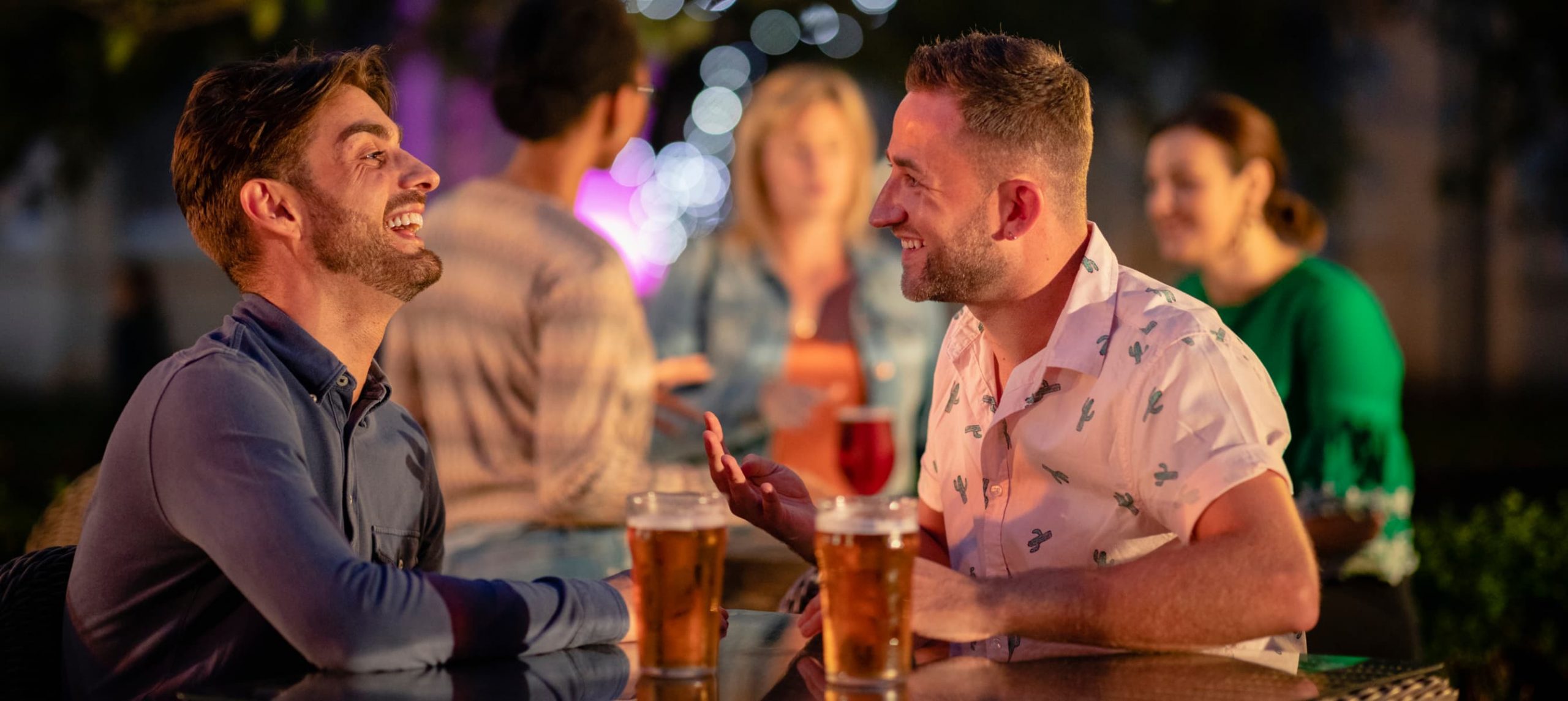 A young gay couple on a date talking happily while drinking beer.