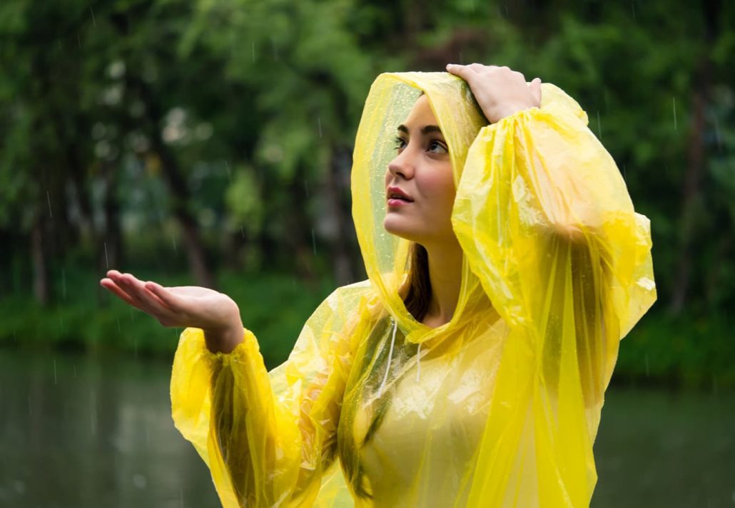Young happy woman in yellow raincoat enjoying the rain