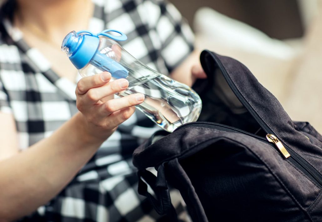 Woman takes the reusable bottle of fresh water with carbon filter out from her backpack.