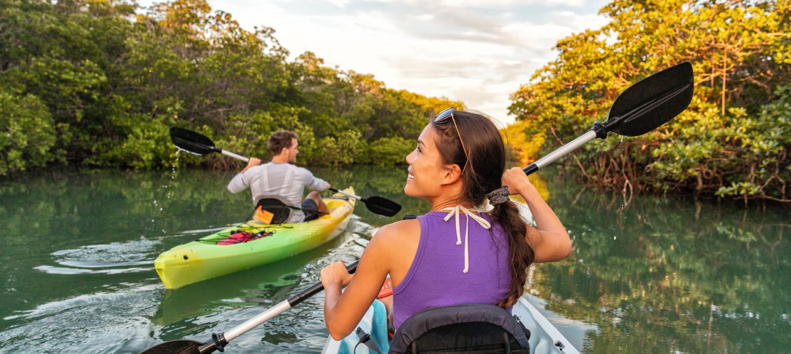 A young woman and her boyfriend happily kayaking on the Florida Everglades on separate boats.