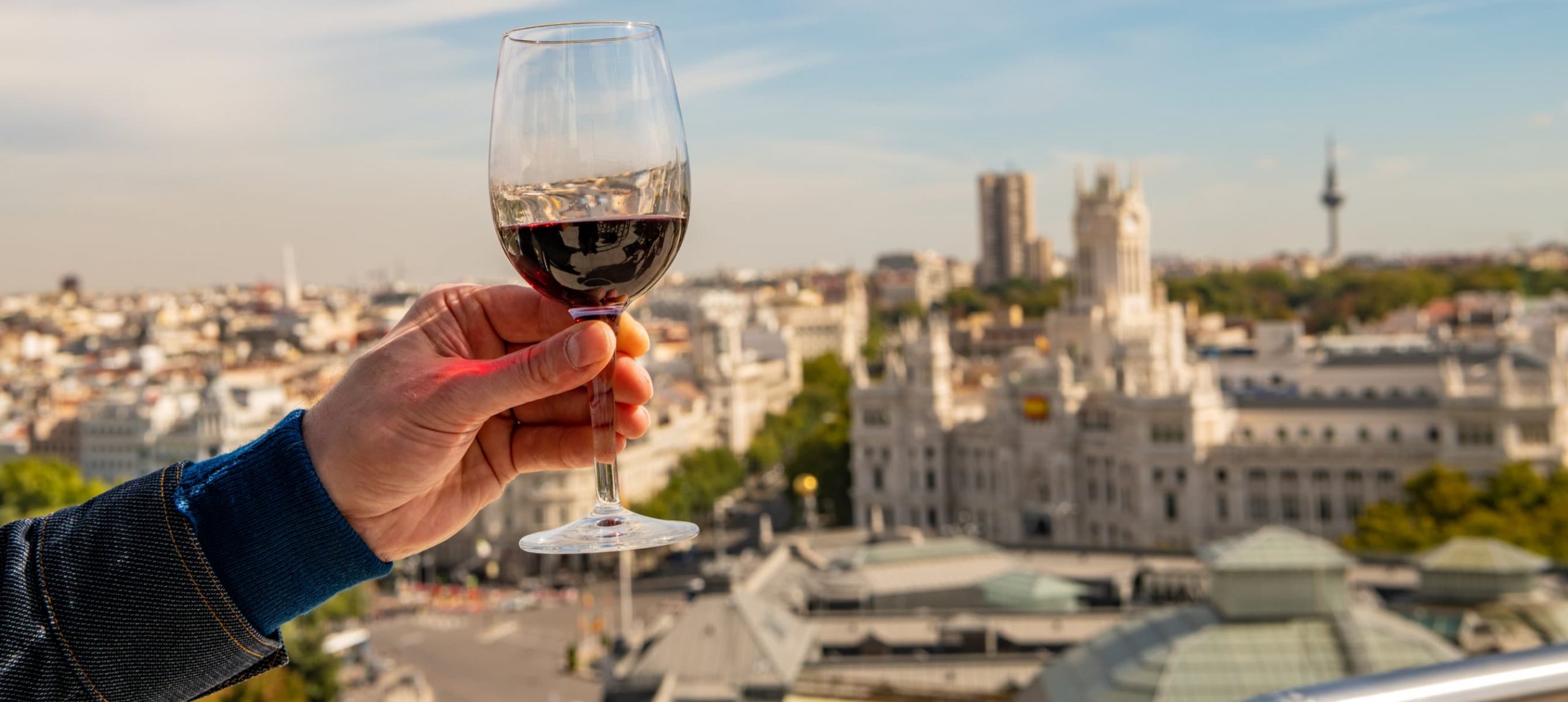 A glass of red wine held up for a toast on a rooftop overlooking the beautiful cityscape of Madrid, Spain.