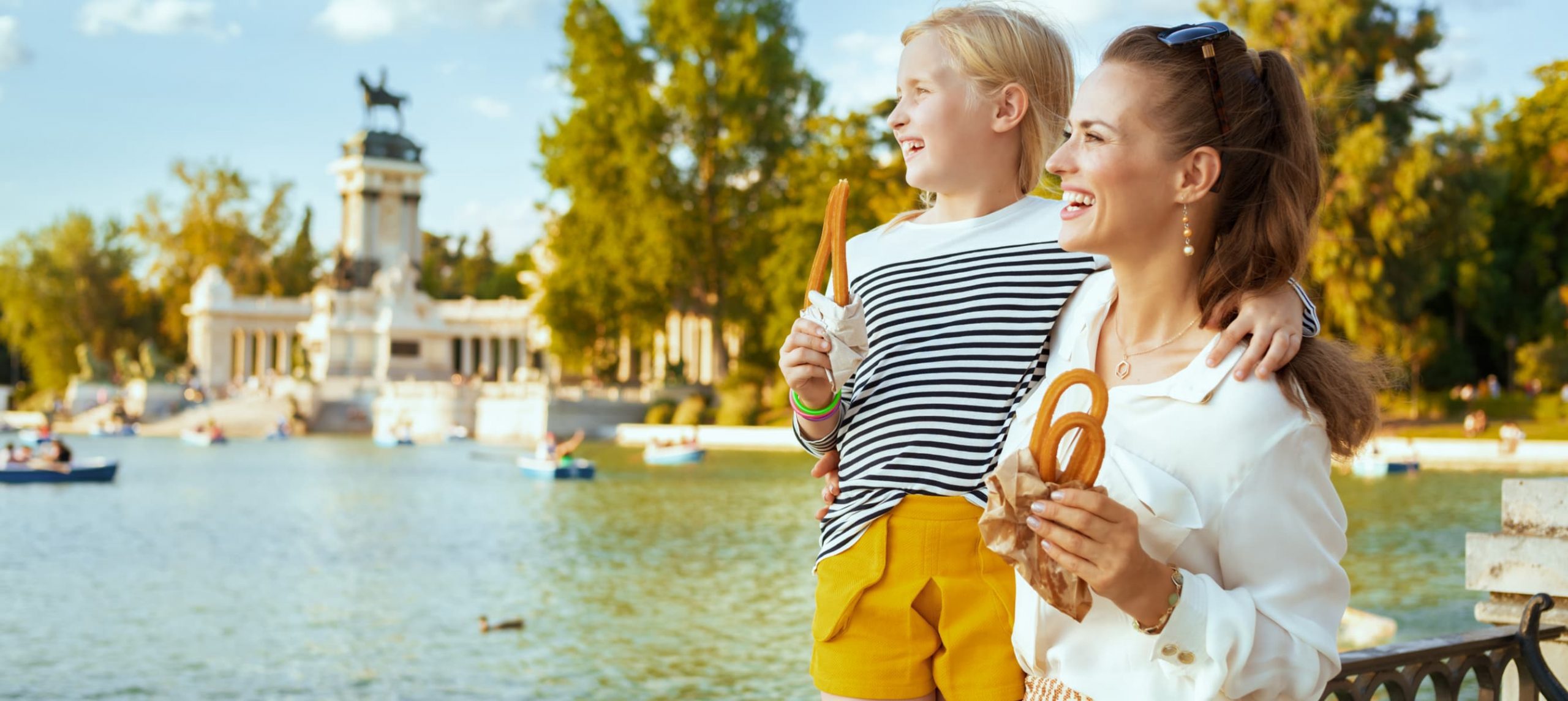 Mother and daughter smiling while eating churros in El Retiro Park, Madrid, Spain.