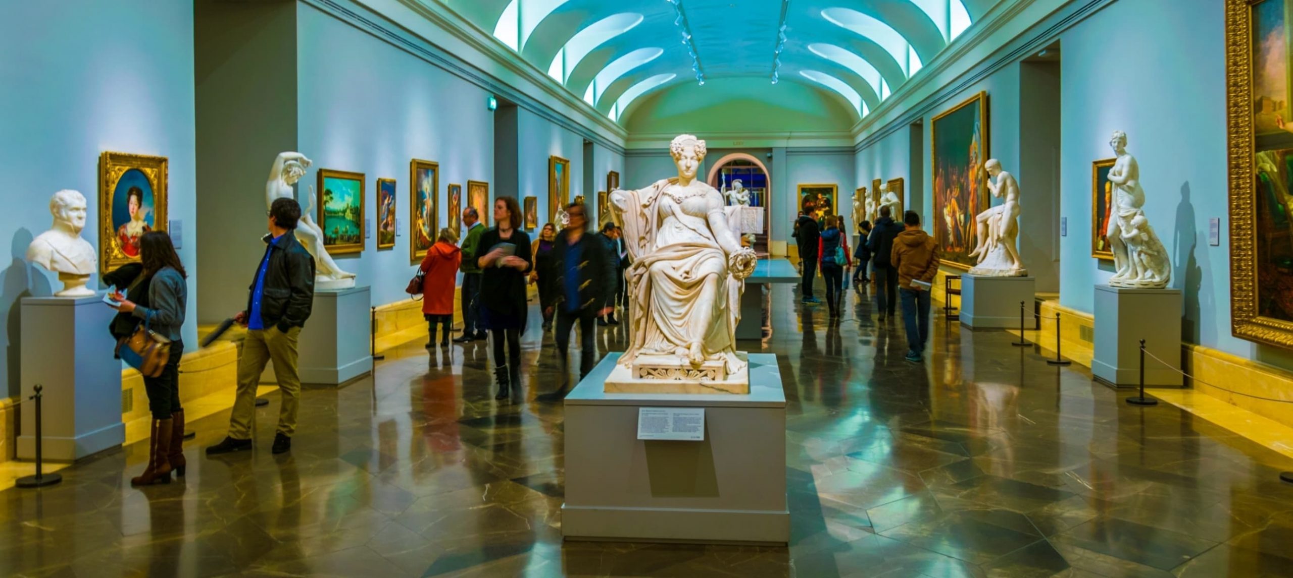 People are strolling through corridors of the Prado museum, Madrid, and enjoying view of painting masterpieces