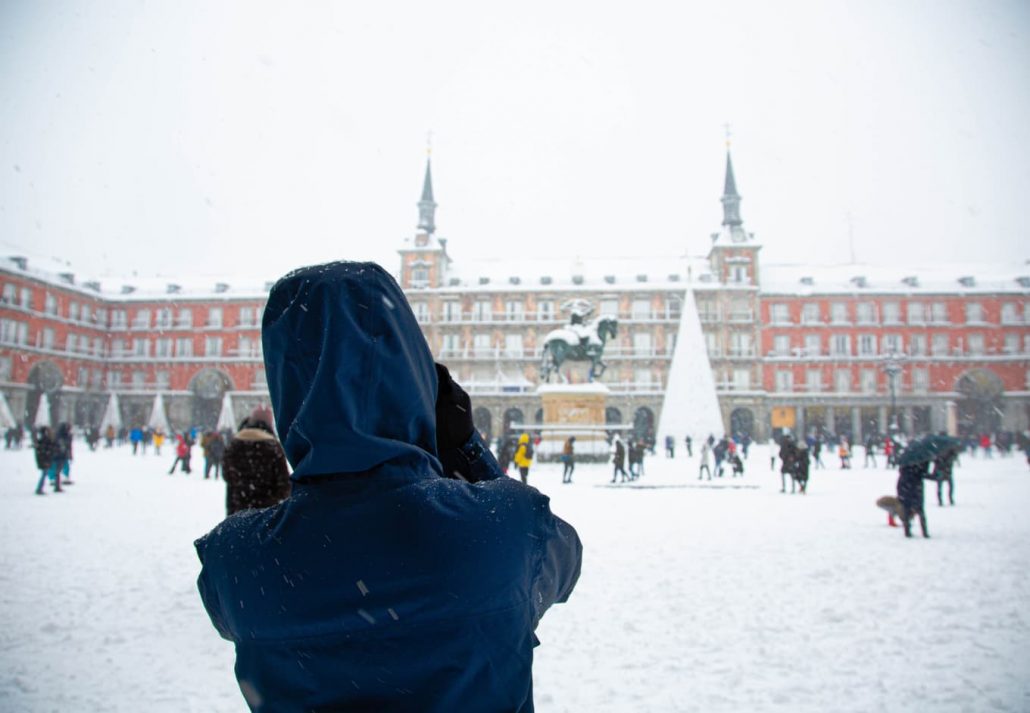 Woman photographing Plaza Mayor covered in snow in Madrid, Spain