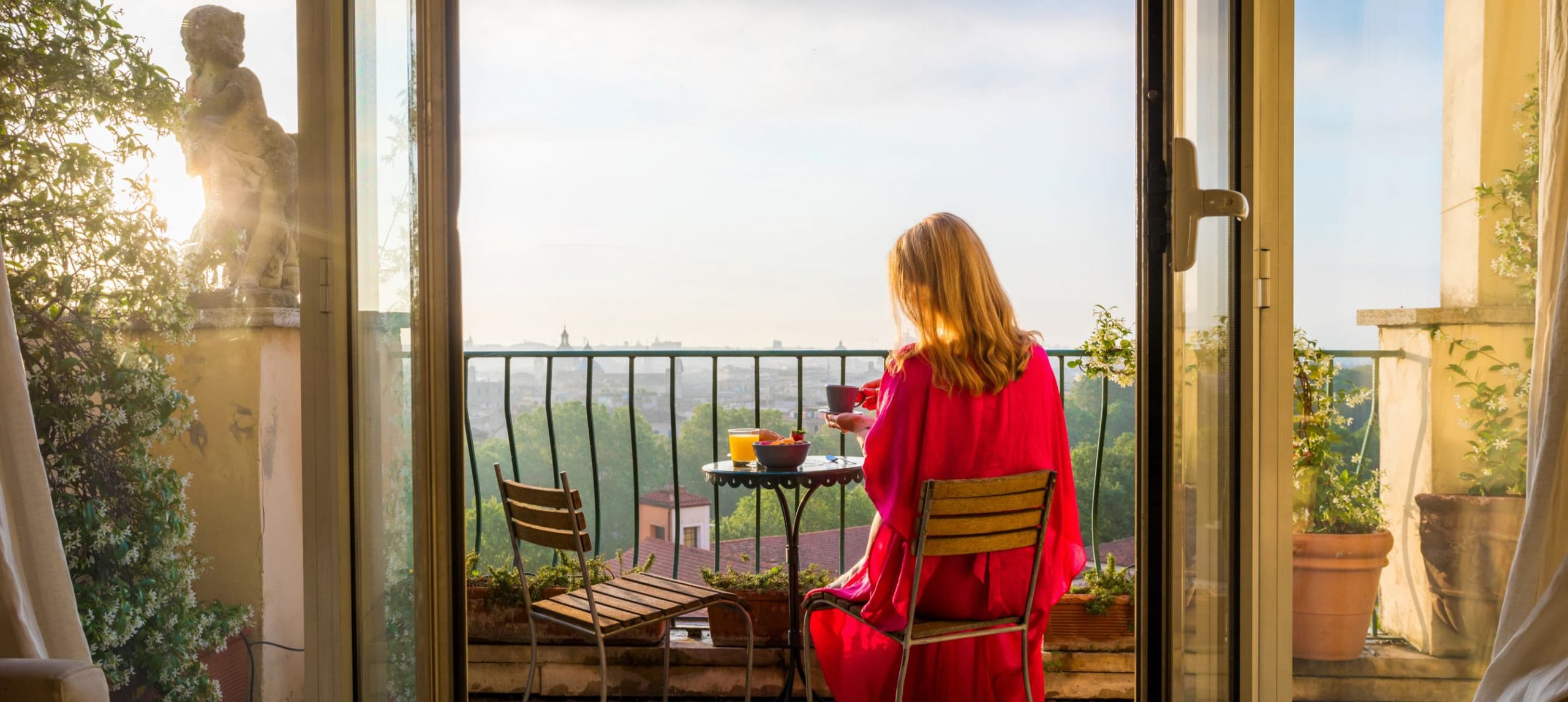 Best Hotels In Rome: Woman sitting on balcony and overlooking Rome during sunrise