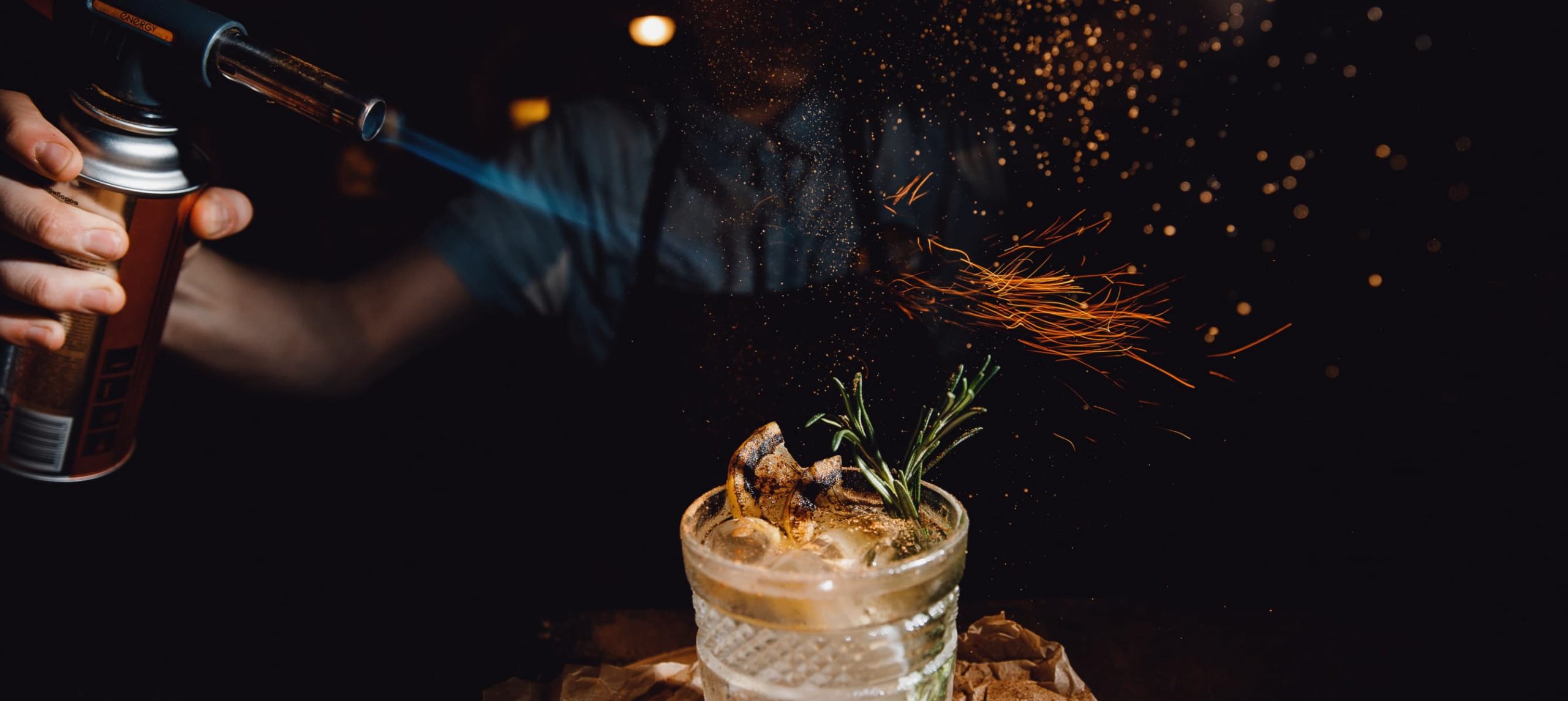 A male mixologist flaming up a cocktail drink in a dark bar