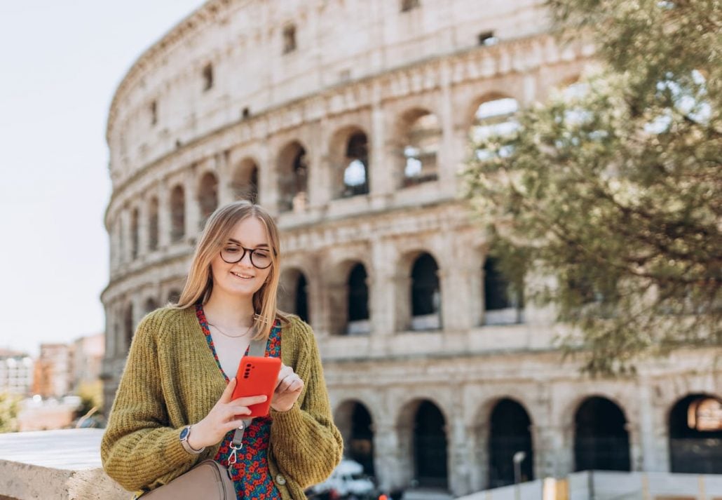 Young woman using her mobile phone in front of the Colosseum, Rome.