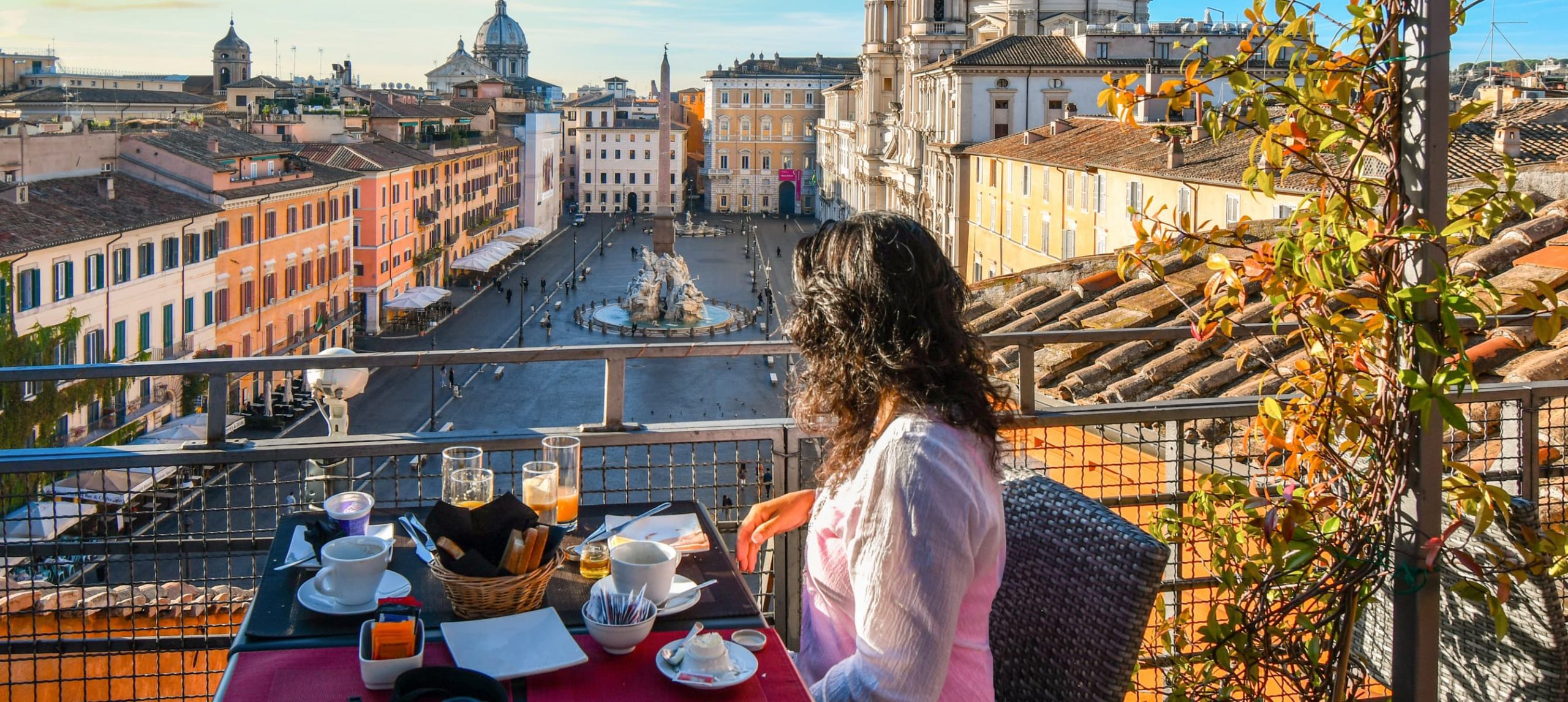young brunette woman sits at a rooftop table after a meal enjoying the morning view of the Piazza Navona in Rome, Italy