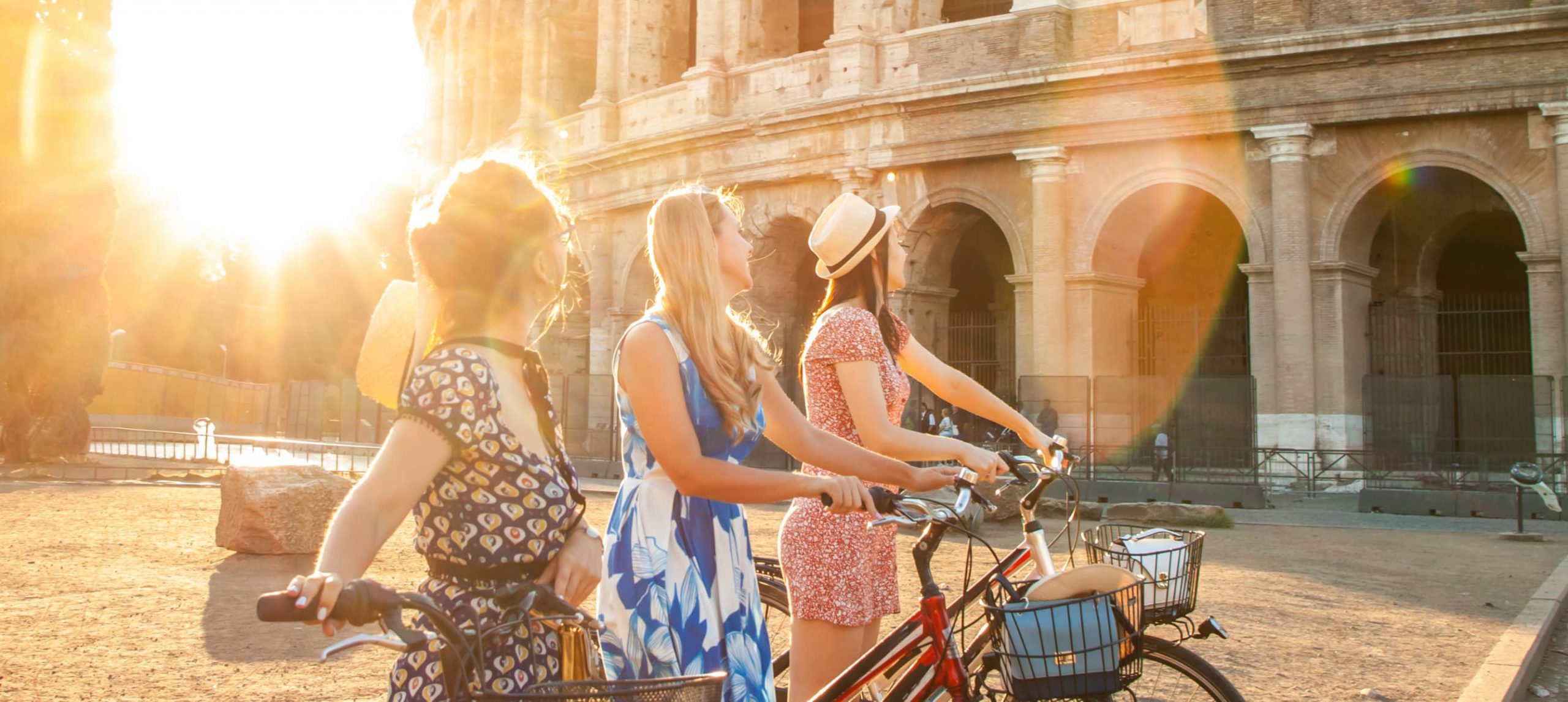 Three young woman biking in front of the Colosseum, Rome.