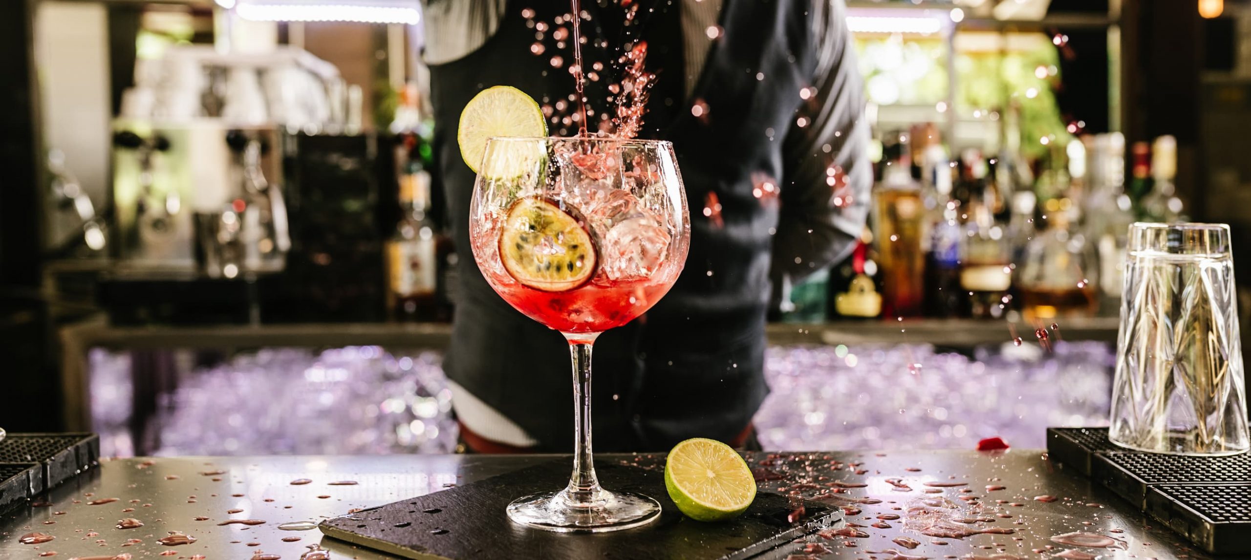 A mixologist pouring a pink cocktail in a glass