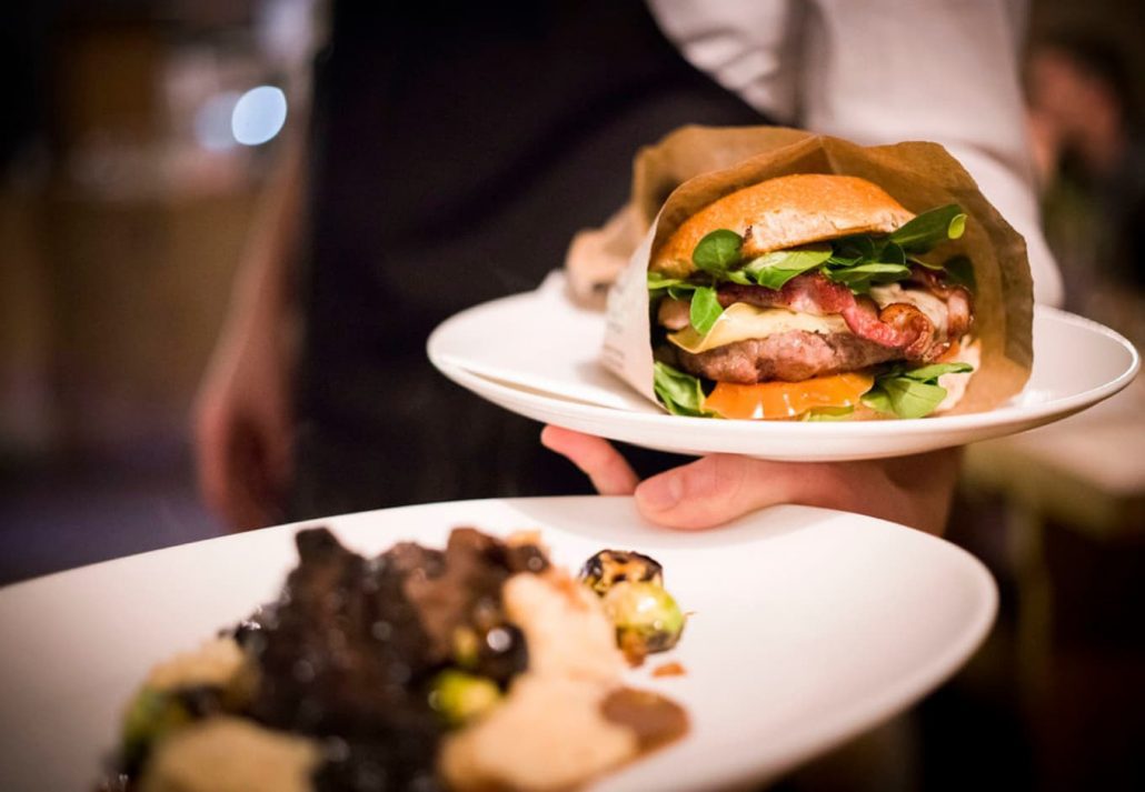 A chef showcasing a burger on a plate at Kumpel and Keule Speisewirtschaft restaurant