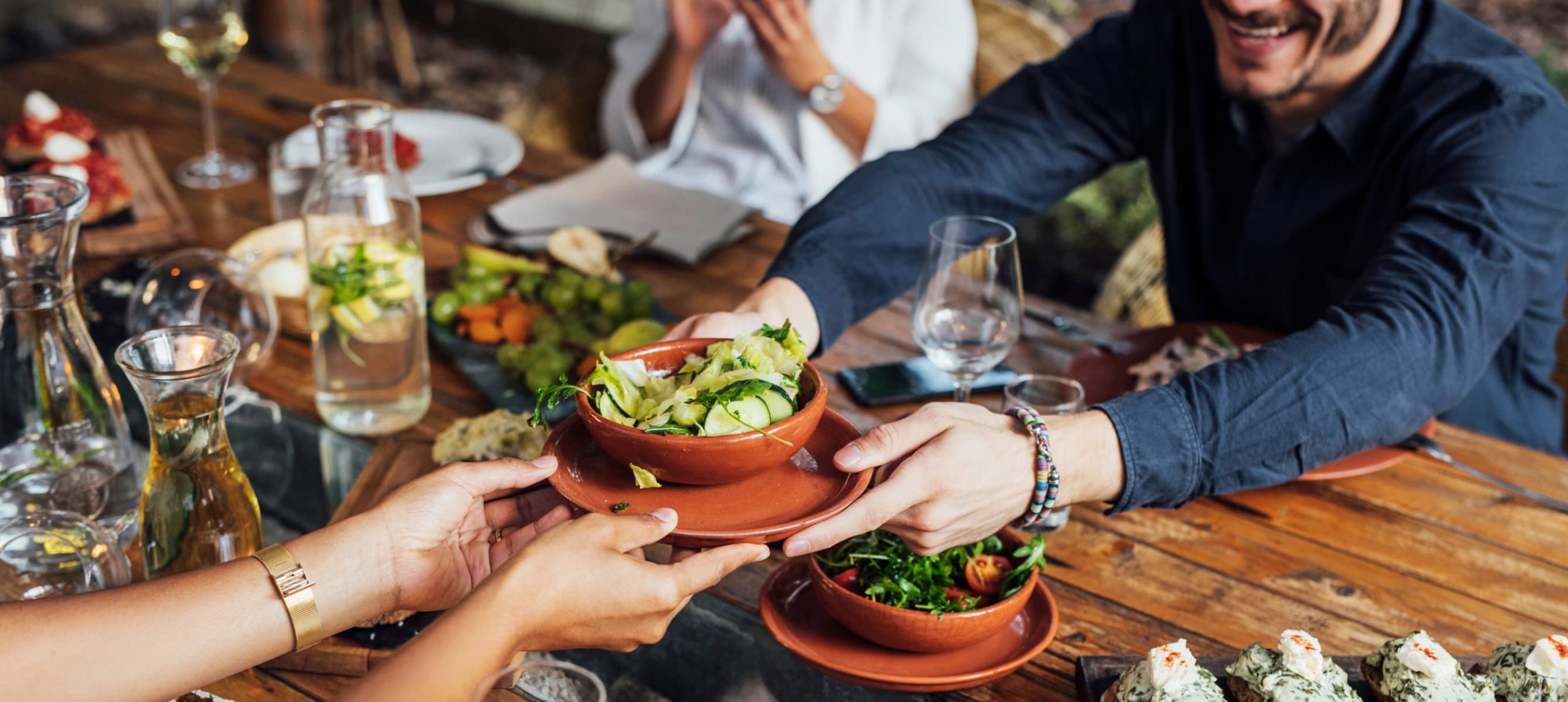 A woman handing over a salad bowl to a man across the table at a restaurant