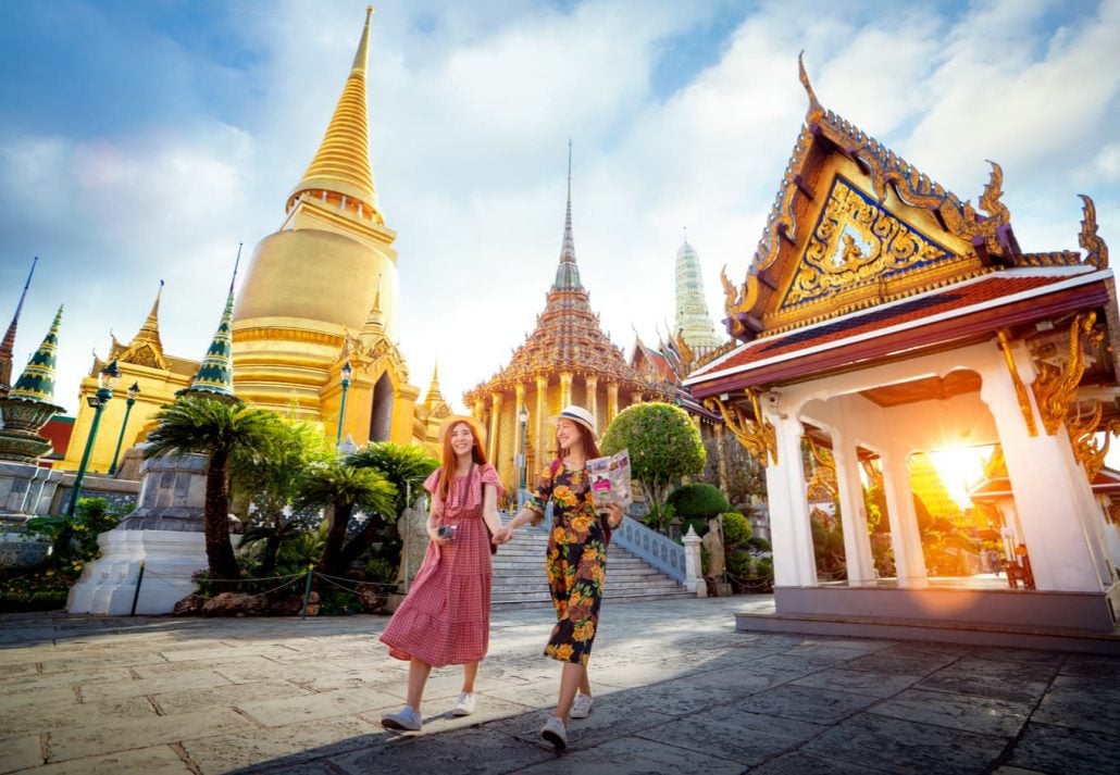 Two young woman walking together in front of a temple in Bangkok, Thailand.