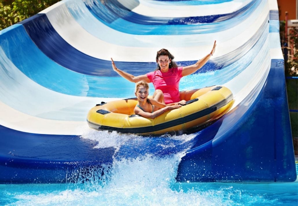 A young boy and his mother gliding down a water slide.