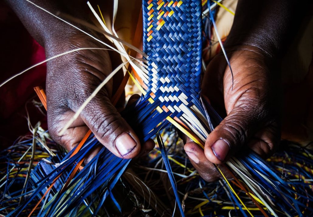 Hands braiding colorful natural fibers during African art making.