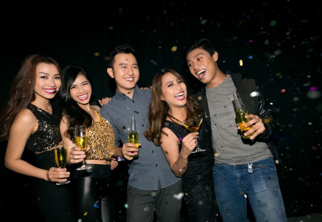 A group of friends smiling at a camera with a drink in their hands