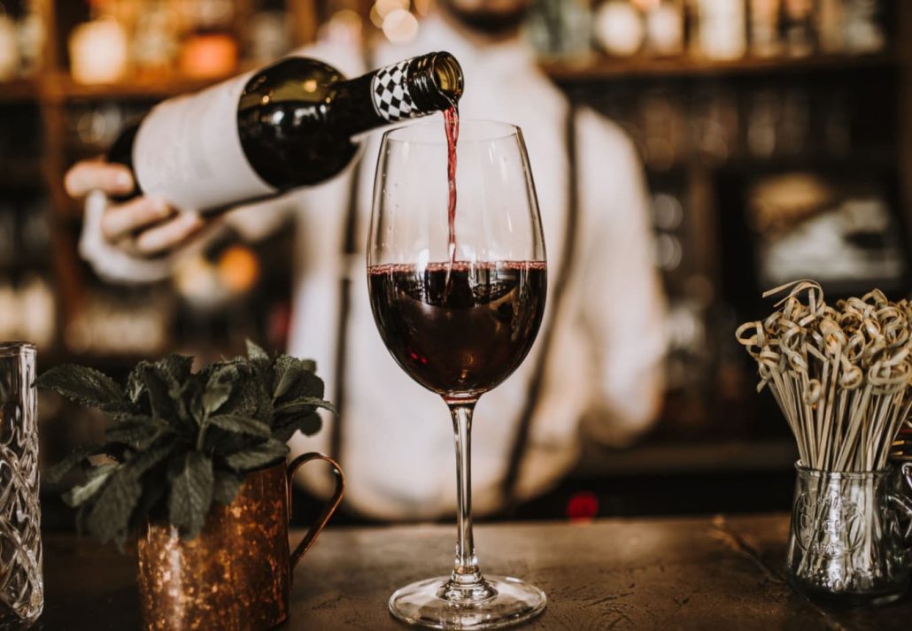 A bartender pouring red wine in a glass