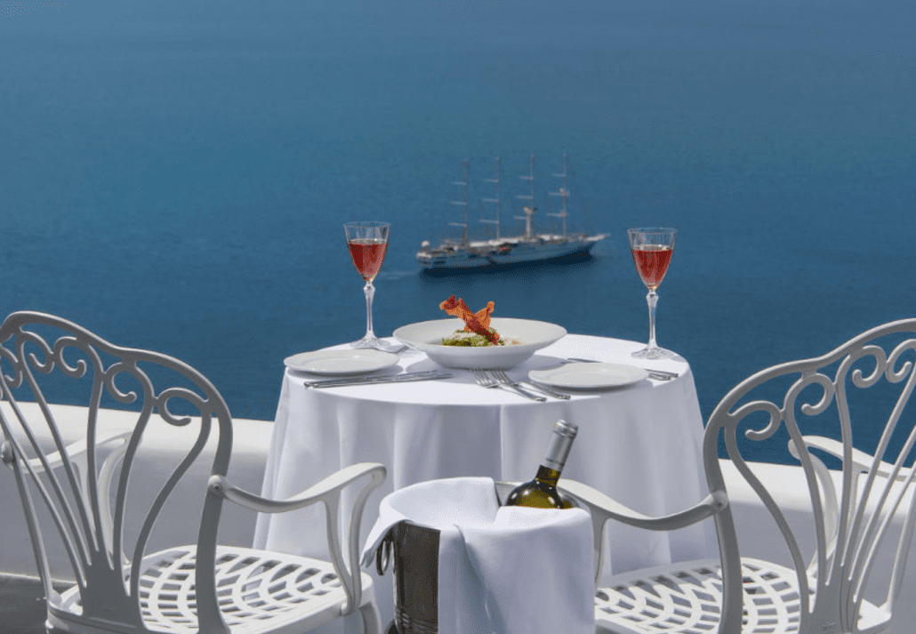 bars_in_greece_esperisma | CuddlyNest Travel Blog Red wine glasses on a white table overlooking the sea in Santorini