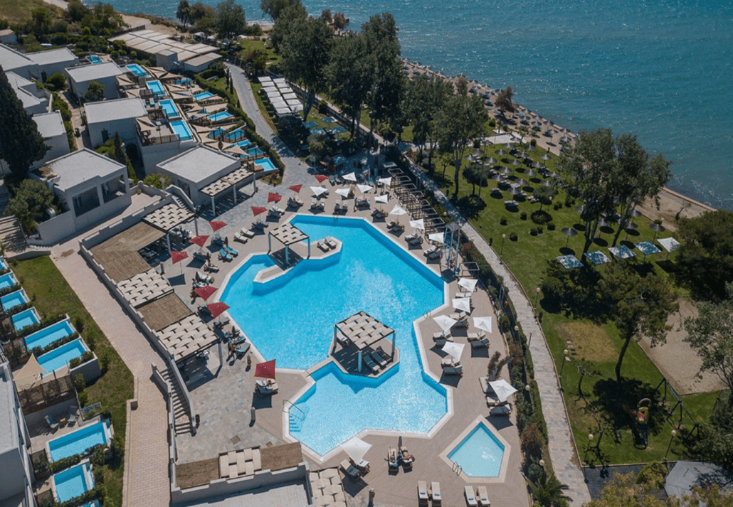 A hotel swimming pool with cabanas and umbrellas near the ocean.