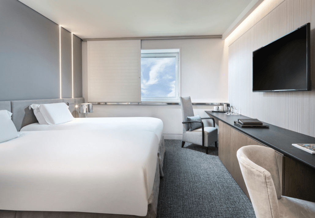 An Athens hotel room with a white bed, a desk, television and a window