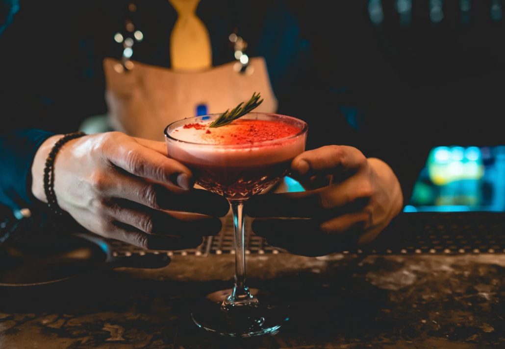 A bartender serving a bright orange cocktail