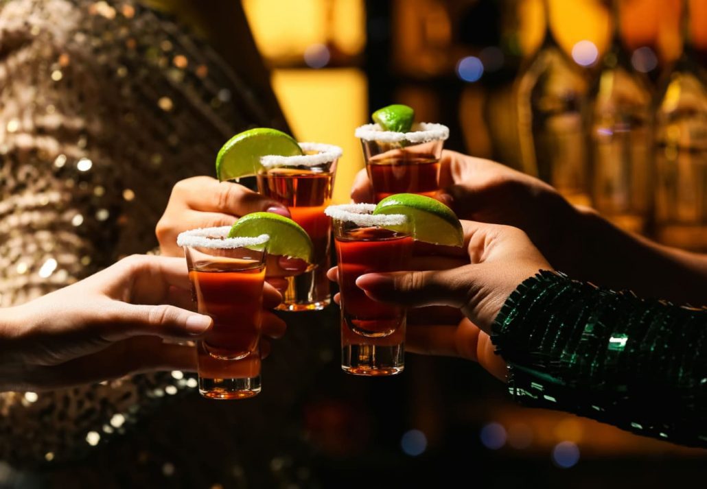 People holding their shots with sliced lime at a bar