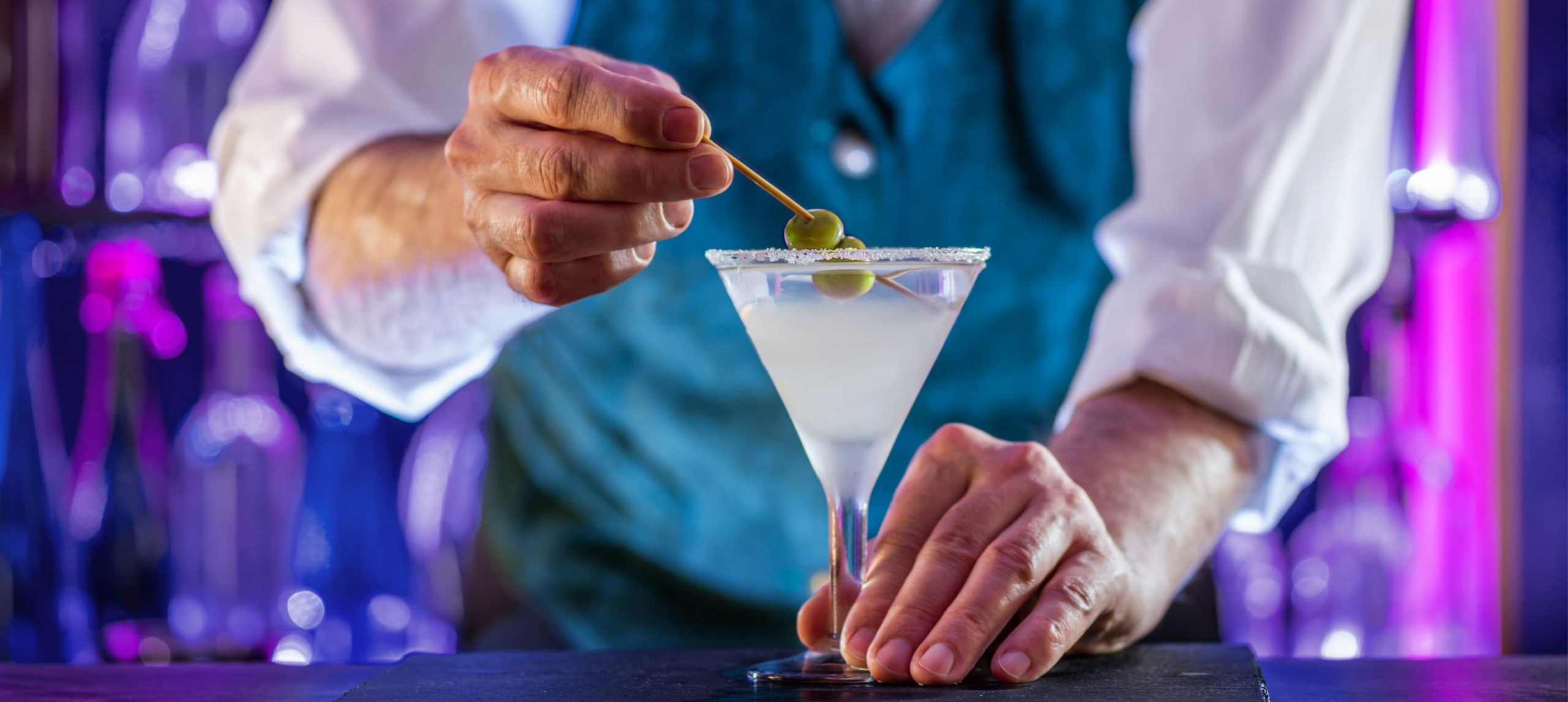 A mixologist putting an olive in a cocktail