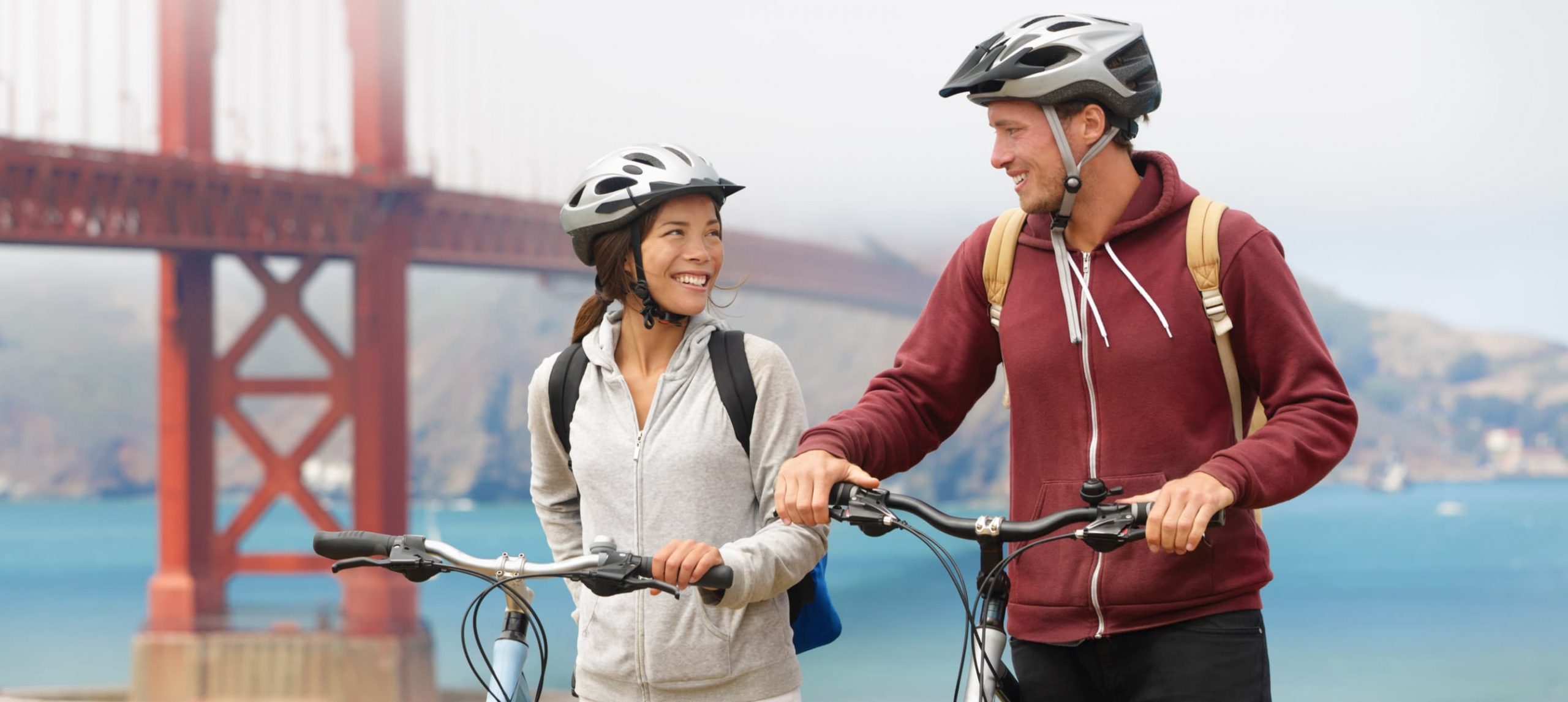 Happy couple biking in front of the Golden Gate Bridge, in San Francisco, California.