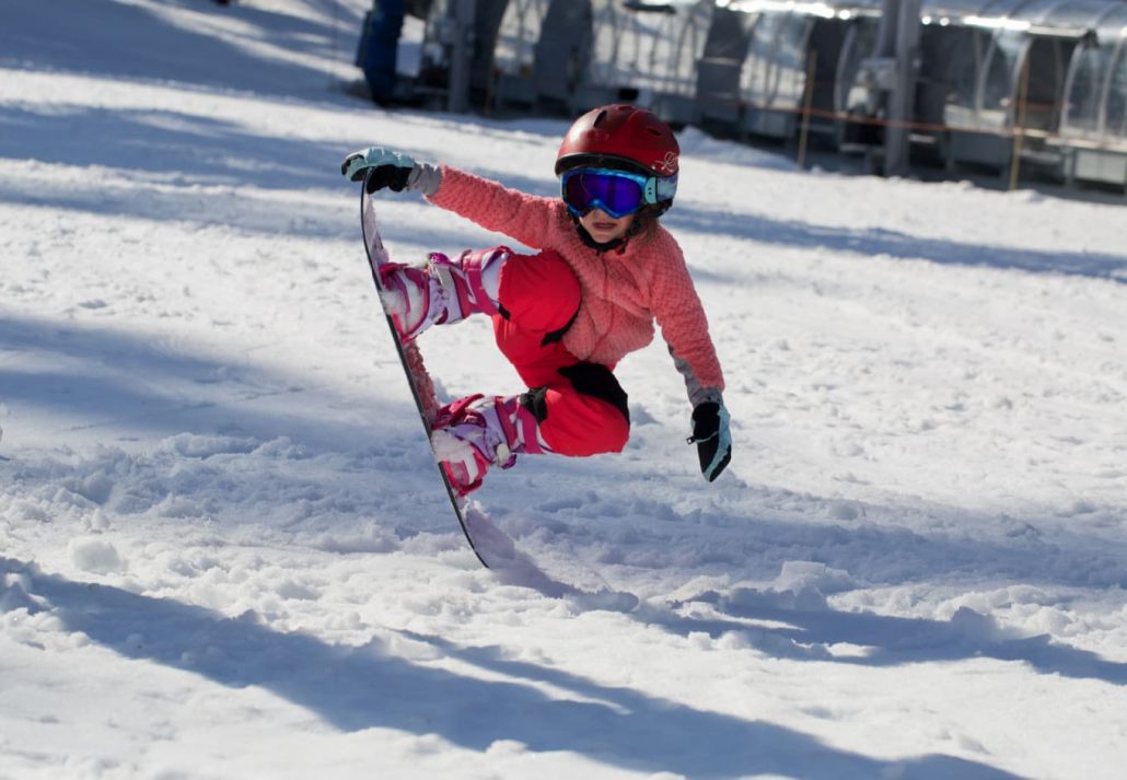 A little girl jumping on a snowboard