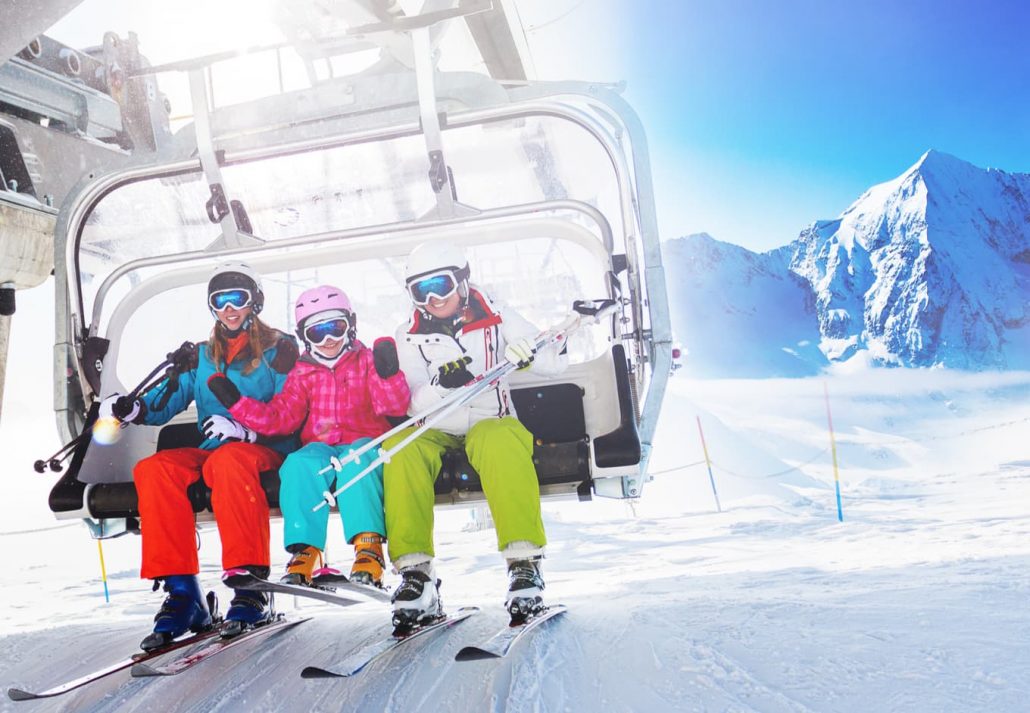 Three people on a ski lift in a snowy ski resort.