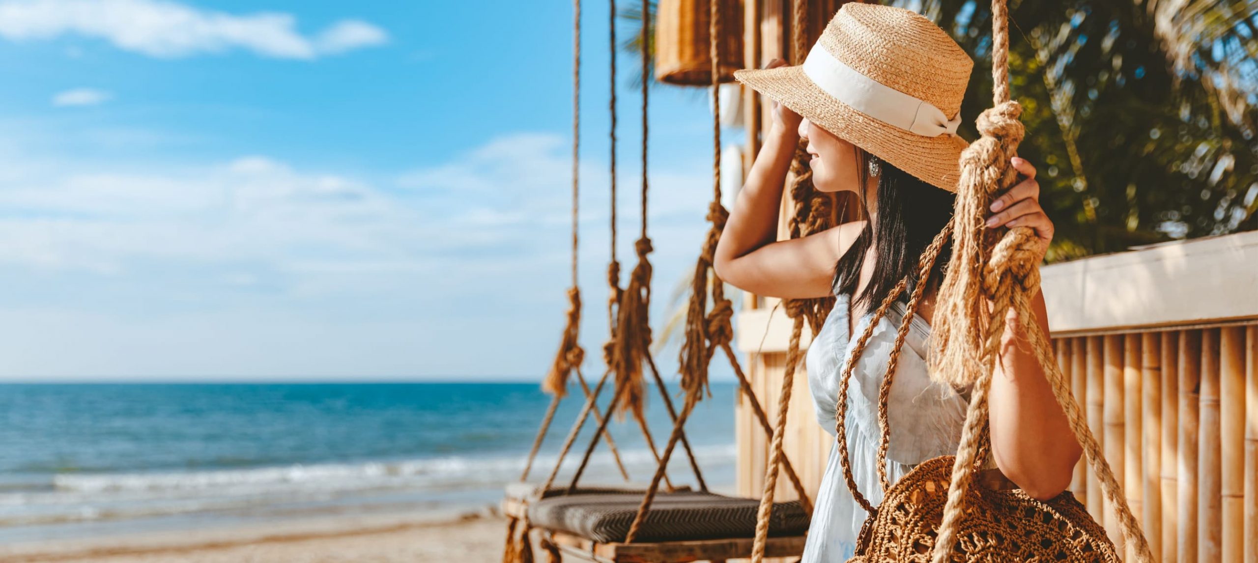 Asian woman sitting on a swing in a beachfront hotel.