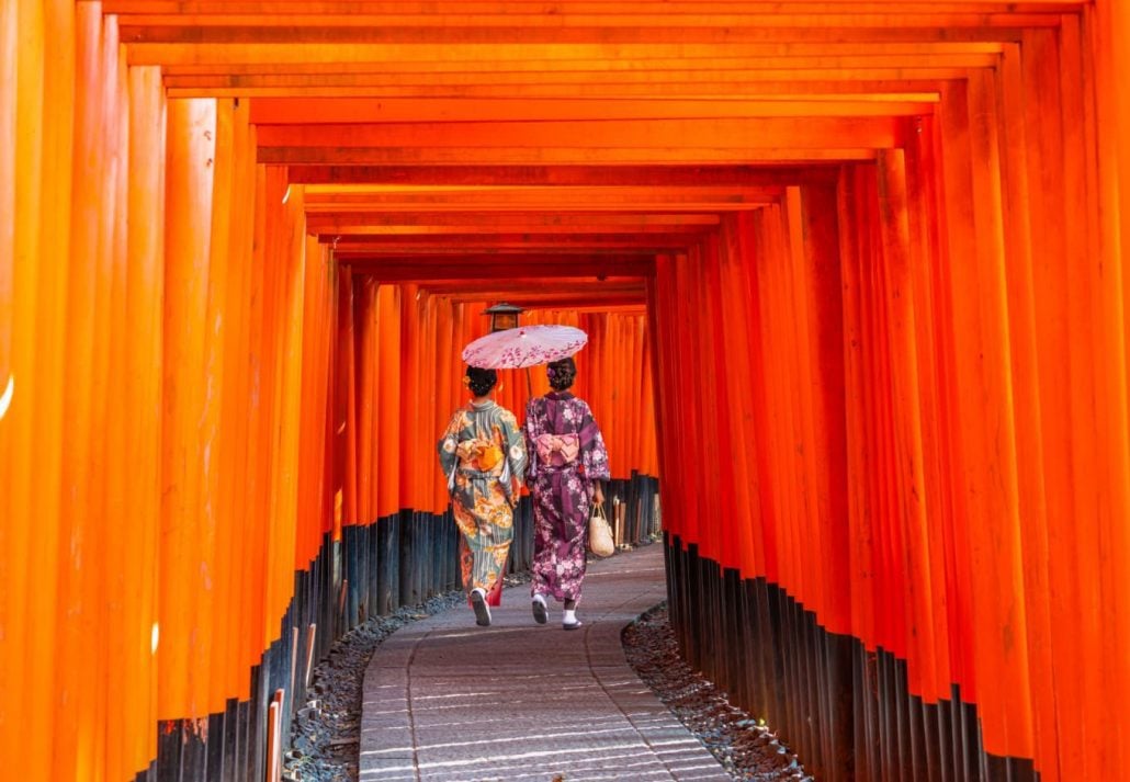 Two young woman dressed in traditional Japanese attire walking through the Fushimi Inari Shrine, in Kyoto.