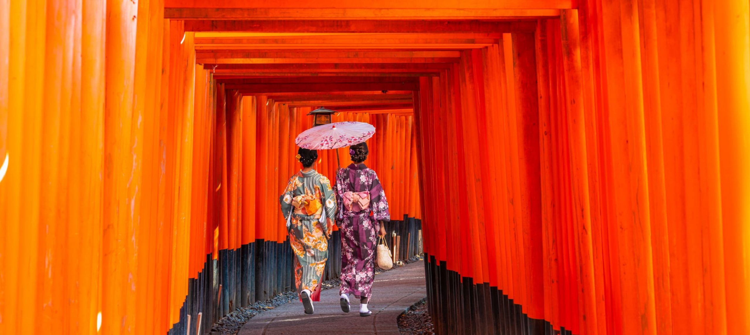 Two young woman dressed in traditional Japanese attire walking through the Fushimi Inari Shrine, in Kyoto.