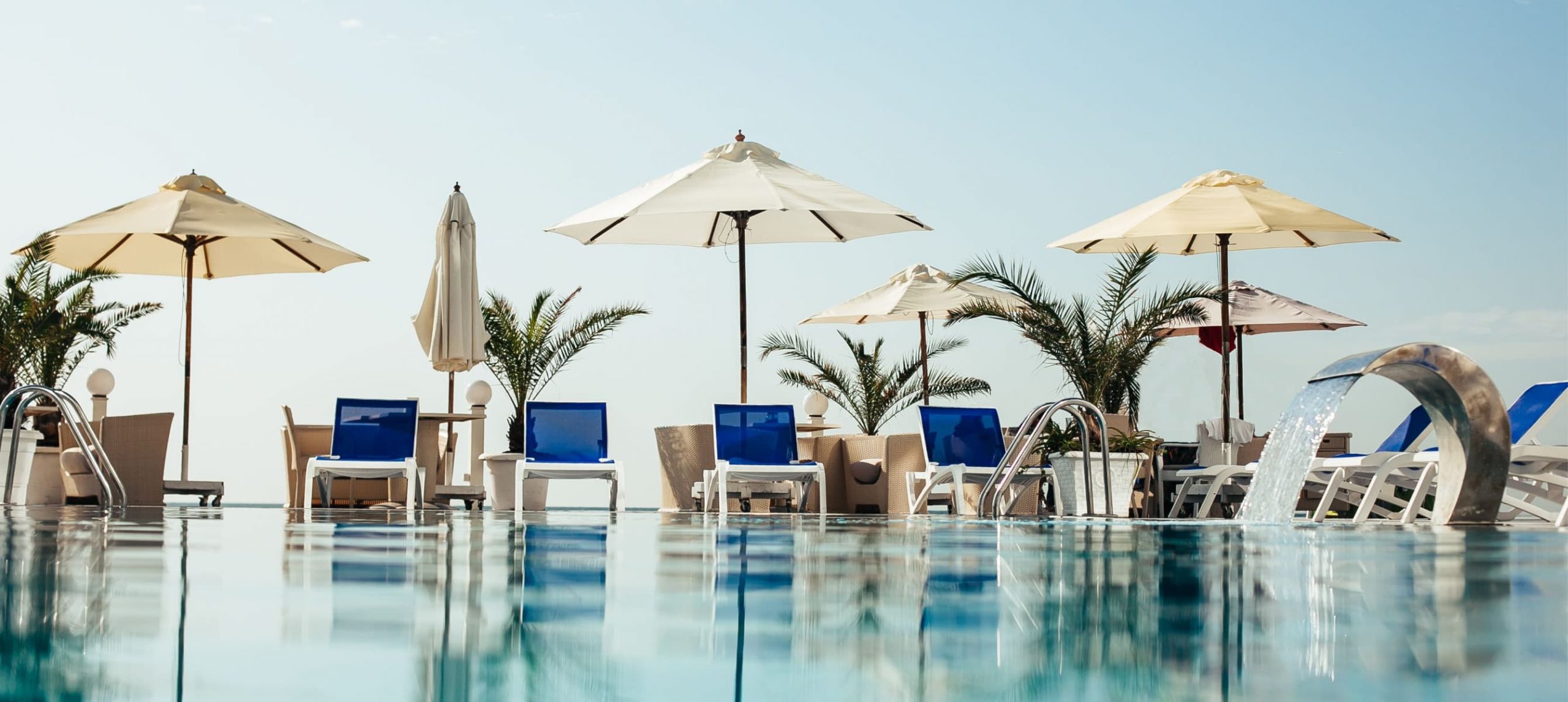 A hotel pool lined with palm trees and subathing chairs.