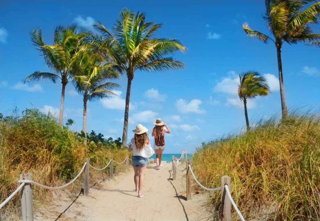 Two young girls running on a sandy path while going to the beach in Miami, Florida.