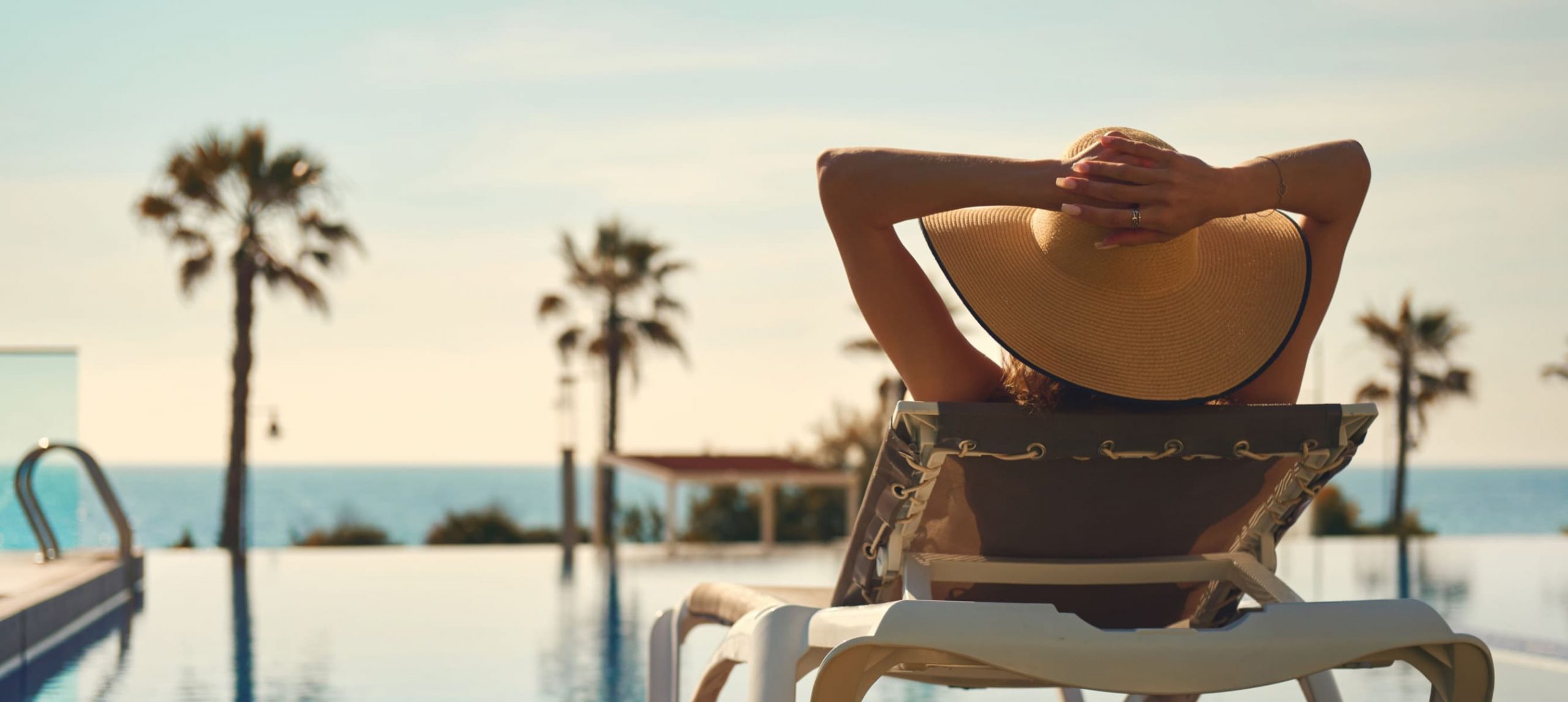 A woman lounging by an inifite swimming pool at a beach resort.