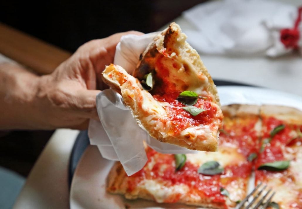 Male hand holding a slice of pizza.