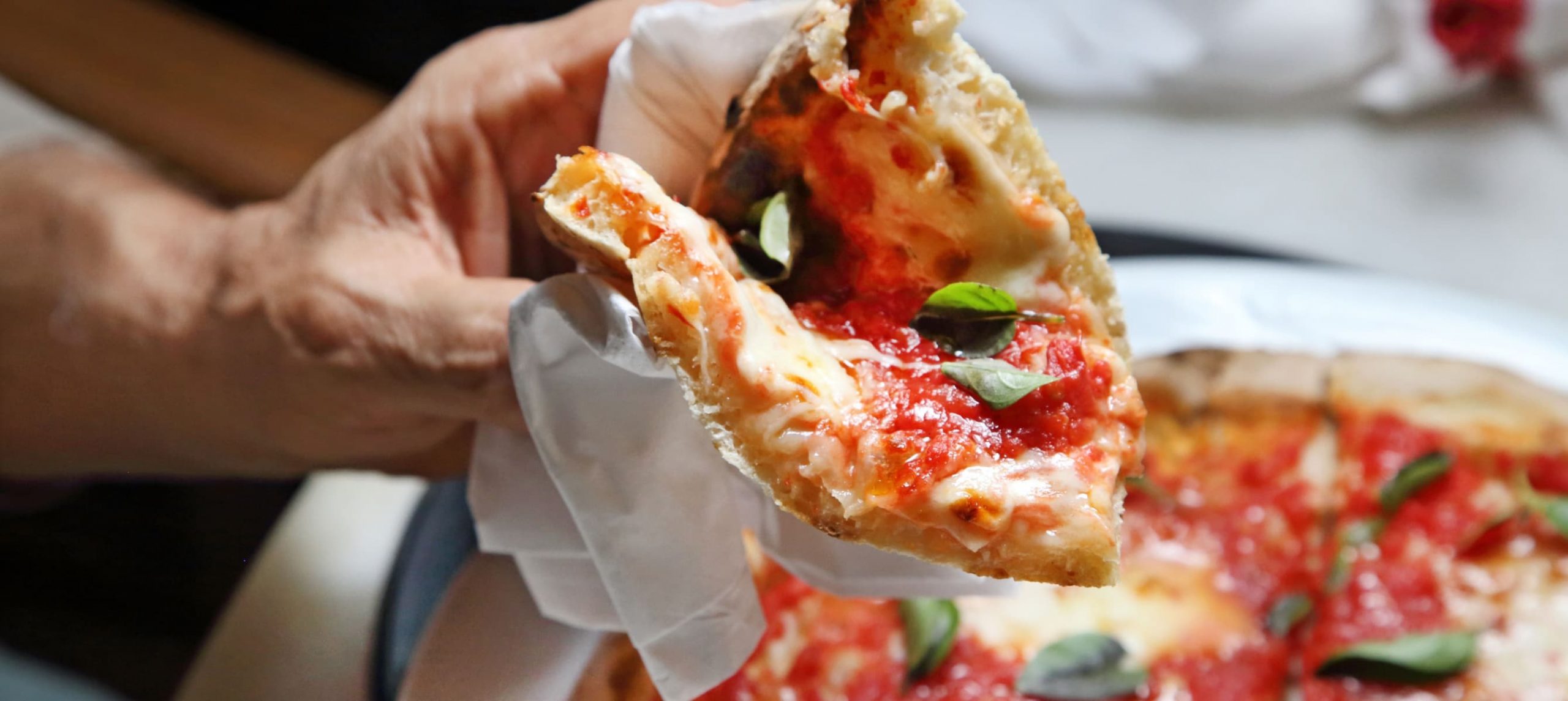 Male hand holding a slice of pizza.