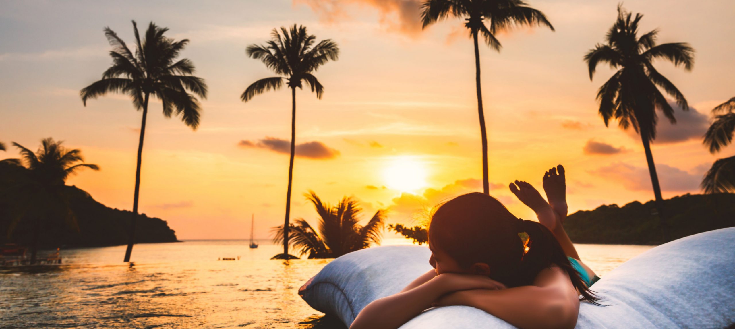 A young woman relaxing in the swimming pool of a beachfront resort at sunset.