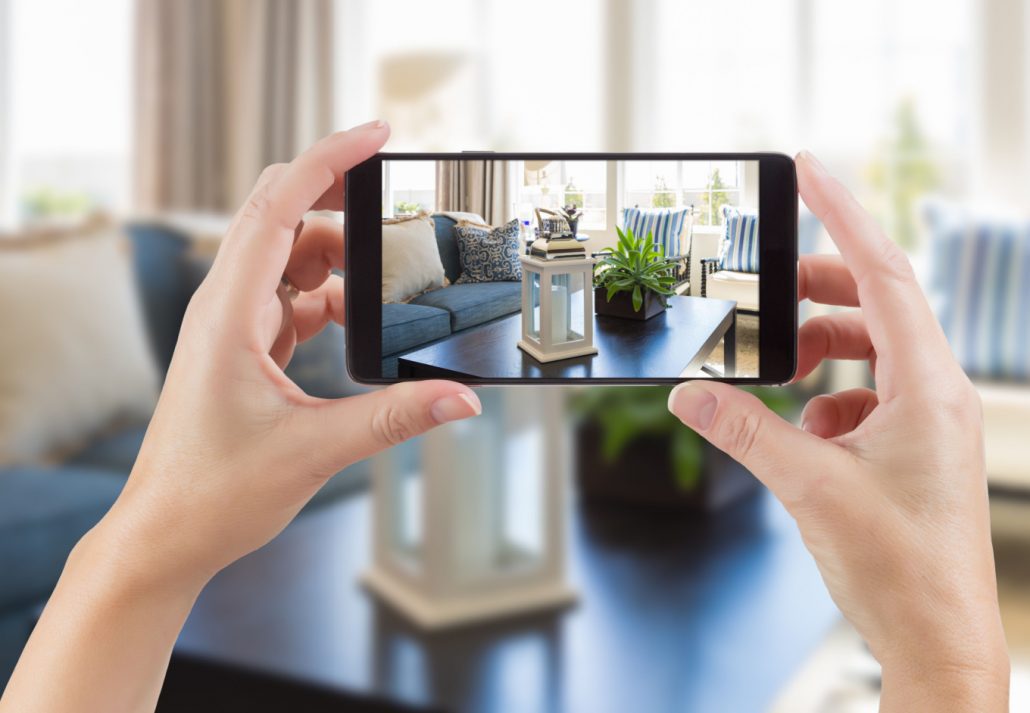 A woman taking a picture of her living room with her smartphone.