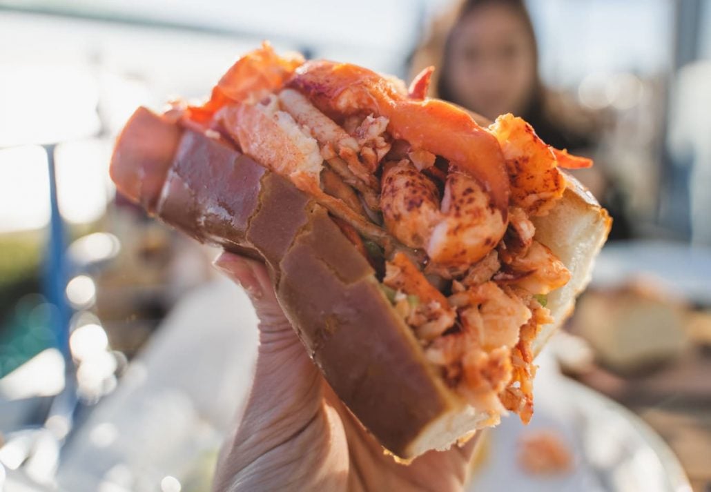 A male hand holding a lobster roll.