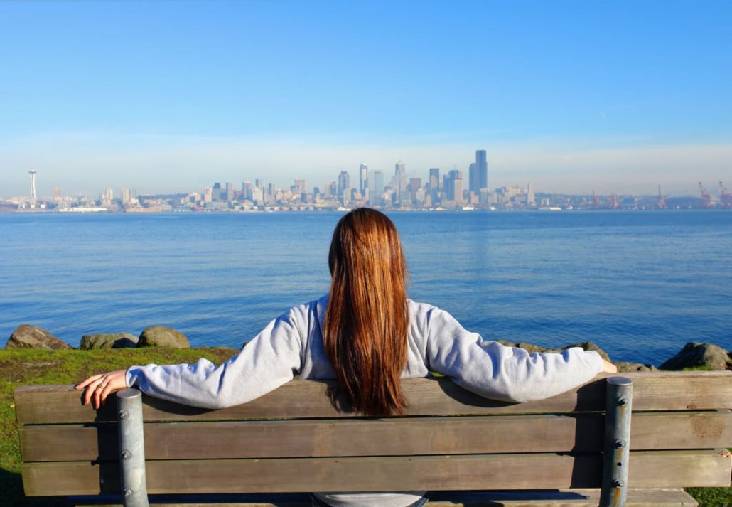 a girl sitting on a bench and looking at the Seattle skyline