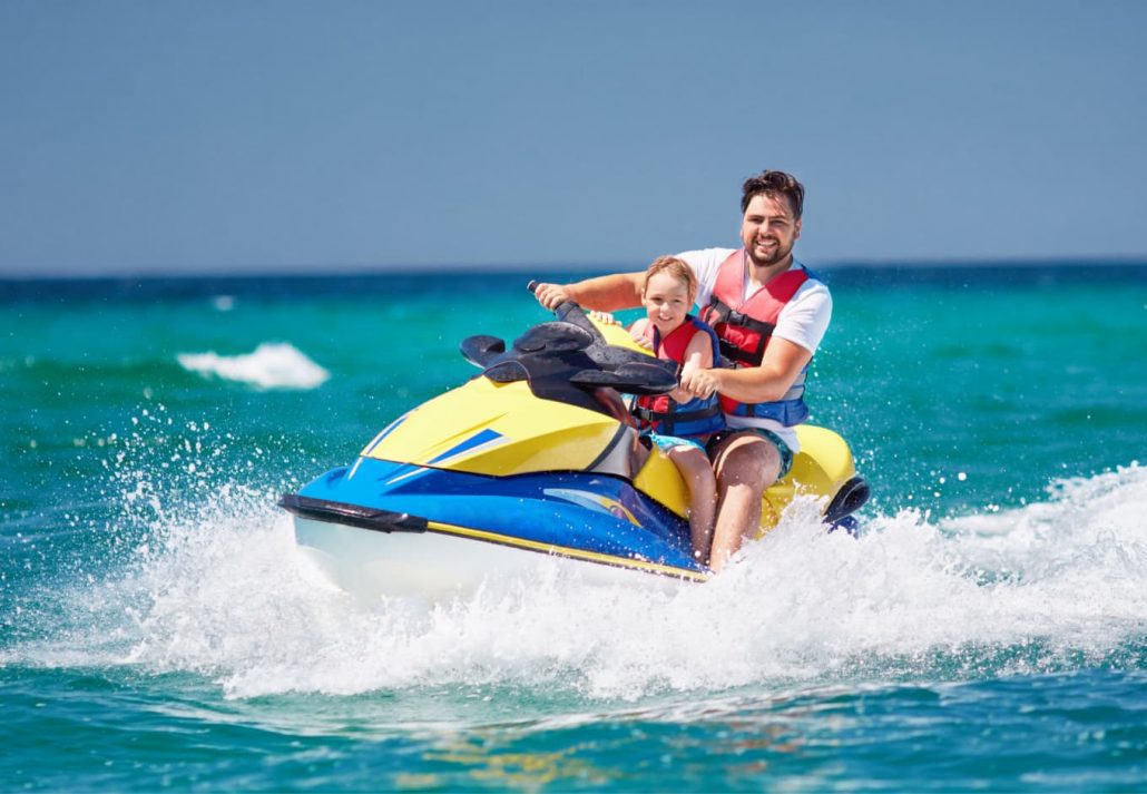 A man and his daughter happily jet skiing in the ocean.