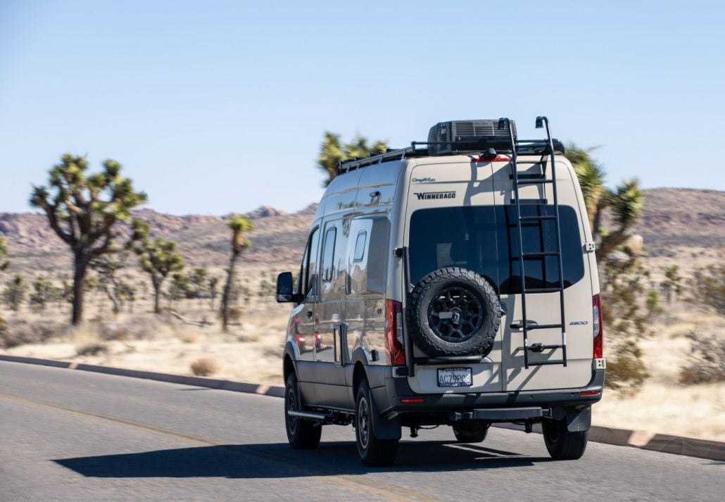 A Winnebago Mercedes Sprinter Van drives through Joshua Tree National Park on a sunny day.
